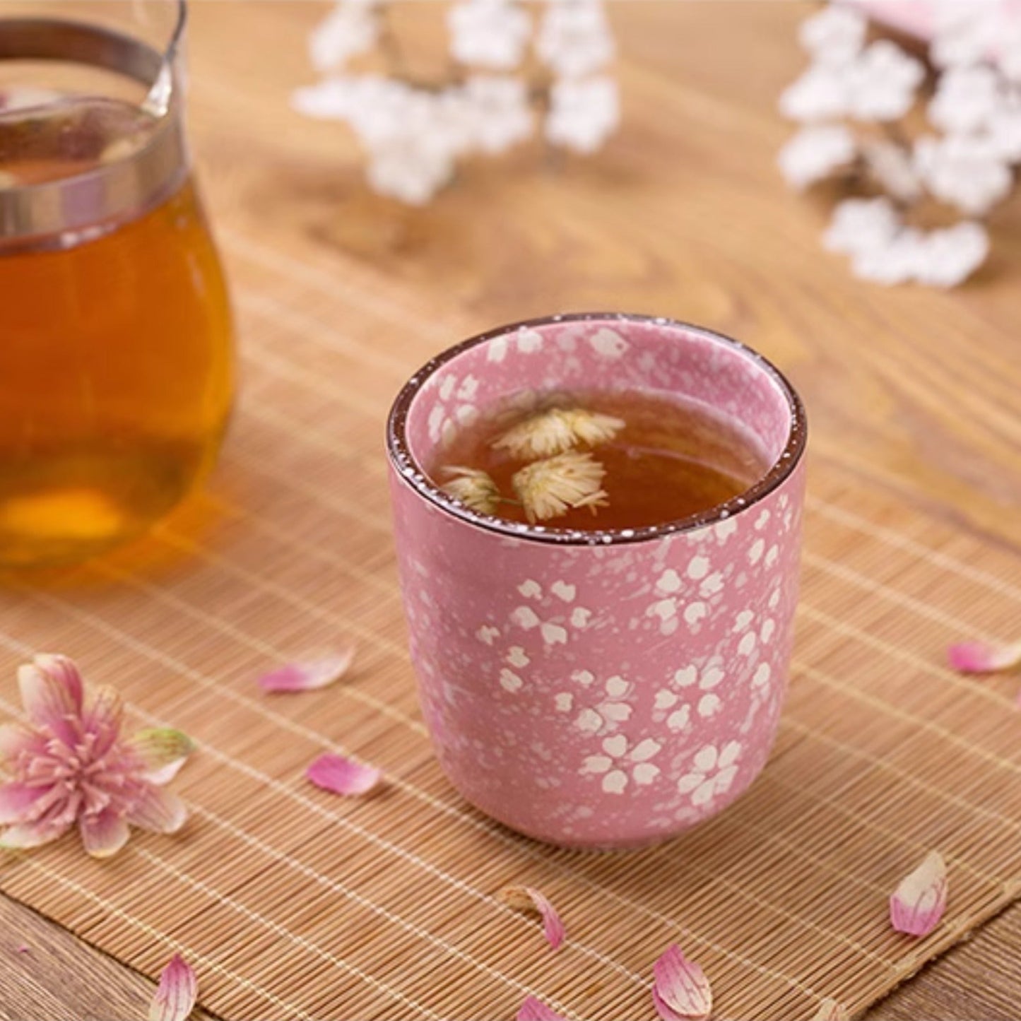 Pink ceramic cup with floral design on a wooden surface with tea and flowers.