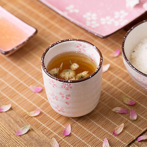 Tea cup with tea leaves on a wooden table with pink petals