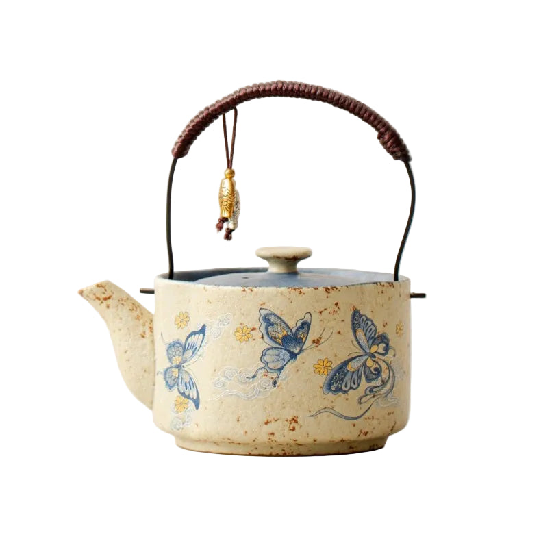 A ceramic Chinese-style teapot with a speckled cream body, blue butterfly and wave motifs, a dark brown woven handle, and a small hanging charm.