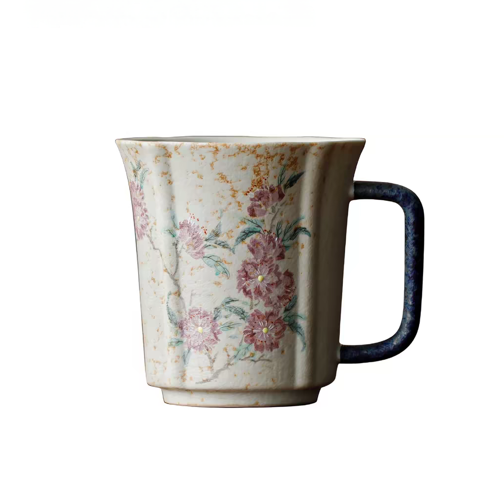 A ceramic mug with a textured cream body, hand-painted pink and green floral motifs, and a dark navy blue handle, shown against a plain white background.