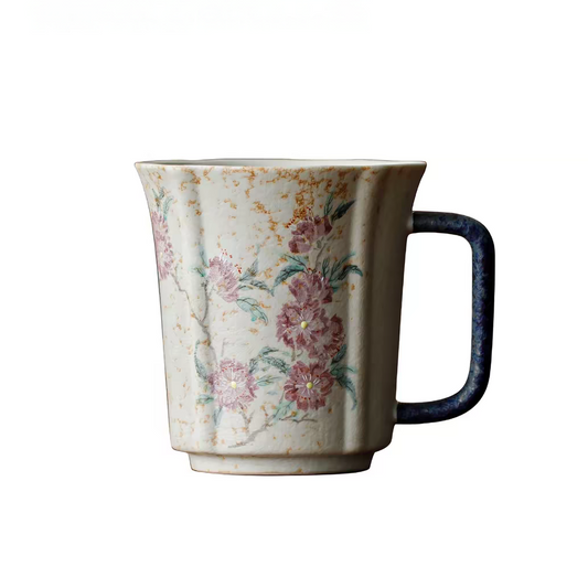 A ceramic mug with a textured cream body, hand-painted pink and green floral motifs, and a dark navy blue handle, shown against a plain white background.